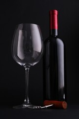 Bottle of wine, corkscrew and glass on dark background