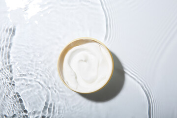 Cosmetic product. Jar with cream in water on light background, top view