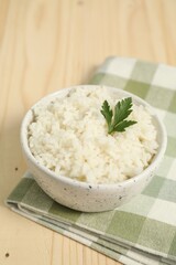 Delicious boiled rice in bowl and parsley on wooden table