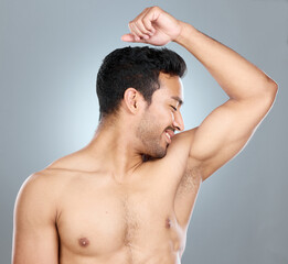 Health, fresh and man smelling armpit in studio for hygiene, clean and wellness routine. Wellness, fragrance and male person checking underarm scent for deodorant or perfume by gray background.