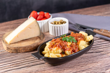 Gnocchi with parmesan cheese on the side in tomato sauce on a wooden table with preparation components around it