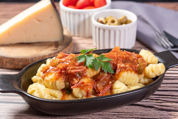 Gnocchi with parmesan cheese on the side in tomato sauce on a wooden table with preparation components around it