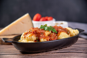 Gnocchi with parmesan cheese on the side in tomato sauce on a wooden table with preparation components around it