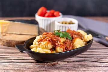 Gnocchi with parmesan cheese on the side in tomato sauce on a wooden table with preparation components around it