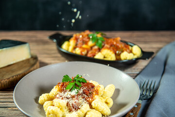 Gnocchi with grated parmesan cheese in tomato sauce on a wooden table with preparation components around it