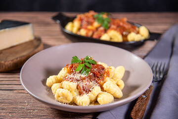 Gnocchi with grated parmesan cheese in tomato sauce on a wooden table with preparation components around it