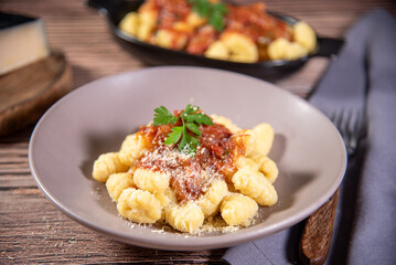Gnocchi with grated parmesan cheese in tomato sauce on a wooden table with preparation components around it