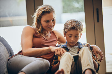 Obraz premium Mother, family and child on tablet and sofa for digital education, playing and bonding at home on school break, Happy woman, mom and boy relax with e learning, teaching and online quiz games or app