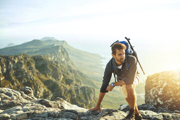 Thinking, climbing and man on mountain with sunset, achievement and rocks on holiday adventure. Nature, inspiration and hiker on cliff with backpack, hiking and trekking on outdoor vacation.