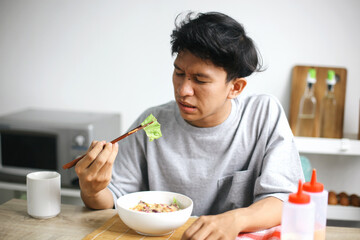 Unhappy Asian Young Man Showing Not Delicious While Holding Vegetable With Chopstick