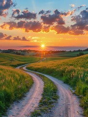 Fototapeta premium A winding dirt road cuts through a vibrant green meadow towards a breathtaking sunset, painting the sky with fiery orange and pink hues