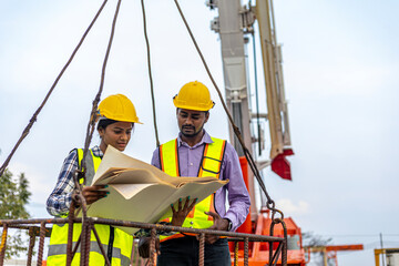 Two civil engineers are in safety uniform standing on a platform checking progress over a construction site