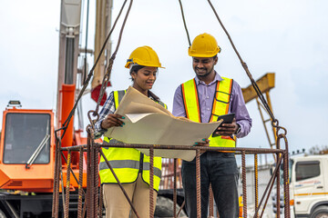 Two civil engineers are in safety uniform standing on a platform checking progress over a construction site