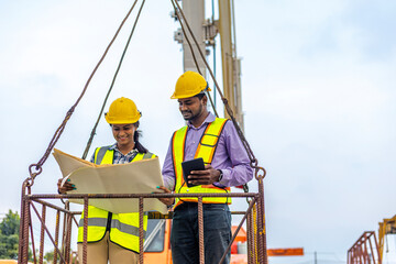 Two civil engineers are in safety uniform standing on a platform checking progress over a construction site