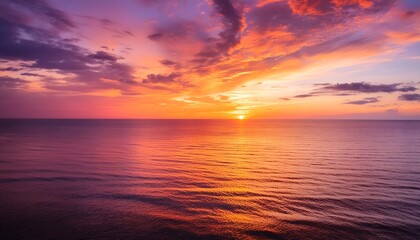 Fototapeta premium Fiery orange sun dips below the horizon, casting long reflections across the rippling ocean waves