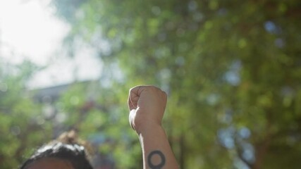 A woman's raised fist with a prominent feminist tattoo in a blurred natural outdoor setting portrays empowerment and activism.