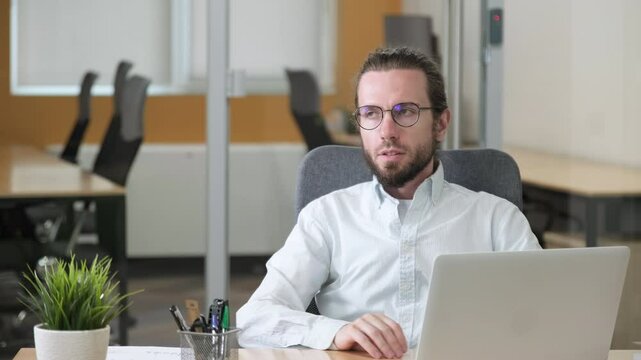 Satisfied businessman with eyeglasses being comfortable sitting on swivel chair, keeping hands behind head in the modern office.