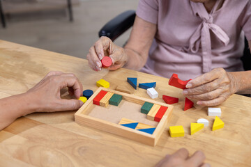 Caregiver and senior woman playing wooden shape puzzles game for dementia prevention