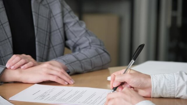 Businessman sitting at desk holds pen signing contract paper. Two hands having a shake hands in slow motion. Close up handshake of business people.