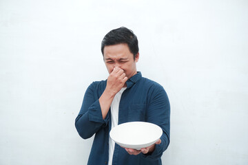 Asian man covering his mouth and nose while holding an empty mockup plate. Covering mouth and nose...