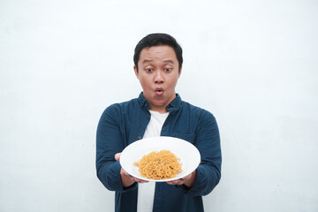 A portrait of happy Asian man wearing a blue shirt excited to eat a plate of fried noodles. Young man smiling and holding a plate of noodle. Isolated with a white background.