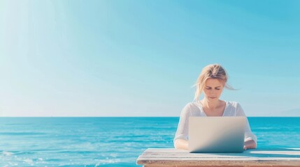 Fototapeta premium Young woman working on a laptop at a wooden table by the sea, under a clear blue sky. Concept of remote work and tranquility.