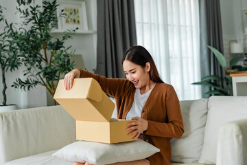Happy young Asian woman opening delivery package at home. Beautiful female customer open box and...