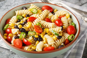 simple hearty salad of fusilli pasta, black beans, tomato and corn close-up in a plate on the table. Horizontal