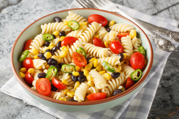 Fusilli pasta with black beans, tomato, jalapeno and corn close-up in a plate on the table....