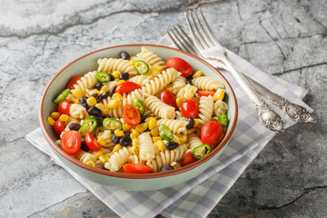 Fresh homemade colorful vegan fusilli pasta salad with beans, corn, tomato and jalapeno close-up in a plate on the table. Horizontal