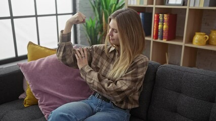Attractive young woman, sporting a confident portrait while flexing fierce arm muscles on living room sofa - a healthy show of strength at home