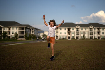 Excited amazed kid boy running on green grass background. Little runners outdoors in summer nature. Sporty child running in a park. Outdoor sports and fitness for children.