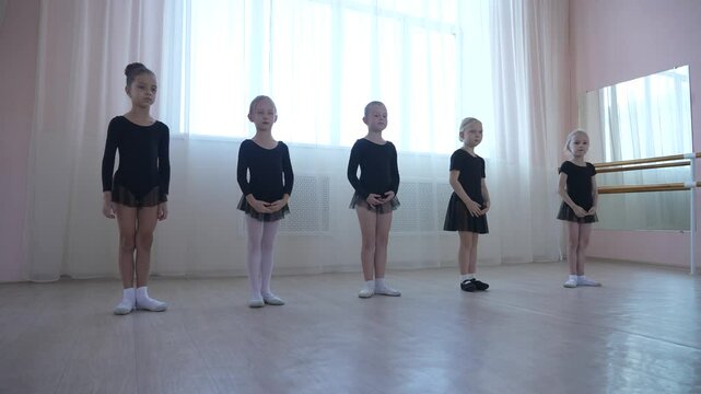 Cute little girls in black swimsuits and tutu practice ballet in class. 