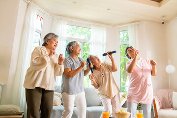 Group of Happy Asian senior women friends singing karaoke with dancing together in living room....