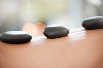 Calm, person and back with hot stone massage at spa for body treatment, wellness and skincare. Resort, hospitality and client with rock for deep tissue healing, holistic and muscle health at hotel