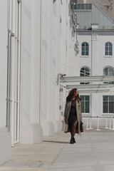 Lady in a trench coat strolling beside a contemporary white building, basking in sunlight. Concept: Reflecting the harmony between personal fashion choices and urban architectural aesthetics