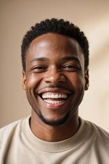 Young african american man with short black hair laughs broadly against beige backdrop