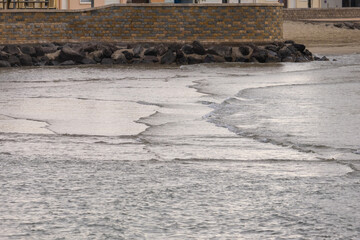 Sea waves on beach with a rocky shoreline and a wall in the background