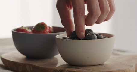 man take fresh strawberries and blueberries in bowls on olive wood board