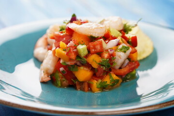 Ceviche salad with shrimps, mango and avocado in a plate on blue background. Latin American food. Delicious, freshly made shrimp ceviche. Shrimp marinated in lime and orange .