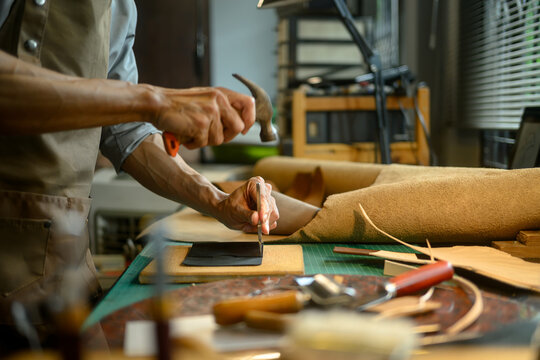 Professional craftsman using a hammer and other tools to shape and detail the leather piece
