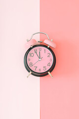 Pastel pink and black alarm clock on light and dark pastel pink background with copy space. Minimal time concept. Flat lay.