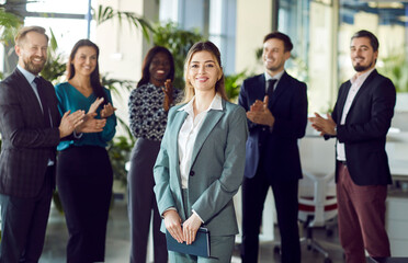 Obraz premium Smiling beautiful female professional leader manager standing looking at camera in office, happy confident business woman corporate leader boss ceo posing, team applauding to support in admire