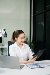  Asian woman with a smile standing holding notepad and tablet at the office..