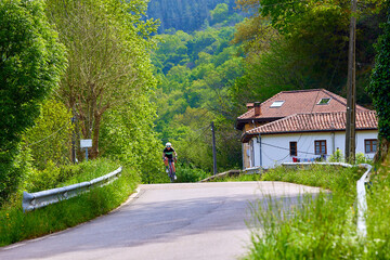 A woman cyclist training on a lonely road on a sunny day wearing a black jersey and bib shorts and a white helmet.