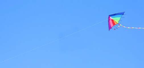 rainbow-colored kite soars through the clear blue sky