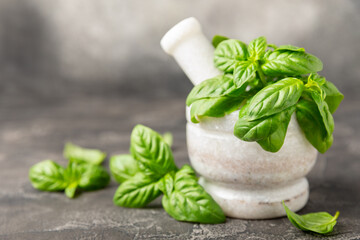 Fresh green basil in a mortar on a textured wooden background. Organic spices and herbs. Vegan. Fresh kitchen herbs. Fresh basil being made into pesto with mortar and pestle.Copy space. Place for text