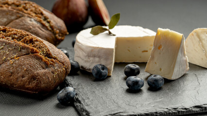 Camembert cheese with figs and blackberries and blueberries on a black wooden table. Wine food and romantic, cheese and bread delicacies.
