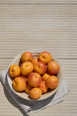 Top view of ripe apricots in bowl on beige striped background