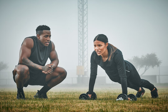 Man, woman and coach with dumbbell on grass for pushup, balance and strong with motivation for wellness. Personal trainer, client and support with training, exercise and guide with plank on field